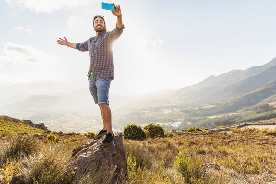 Portrait of man with beard smiling in the camera while taking selfy while hiking in the hills. Franschoek, South Africa