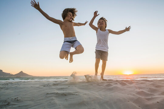 two young kids playing on the beach at sunset