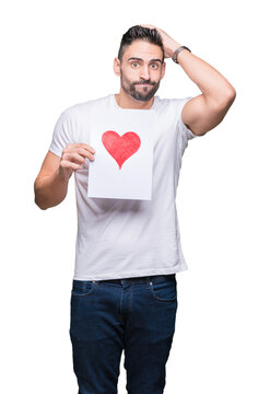 Handsome young man holding card with red heart over isolated background stressed with hand on head, shocked with shame and surprise face, angry and frustrated. Fear and upset for mistake.