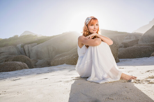 Beautiful woman with red hair in white dress dancing and having fun on the beach with kite. Cape Town, South Africa