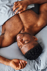 top view of young african american man with muscular body sleeping on grey bedding in morning