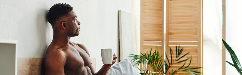 pensive shirtless african american man with coffee cup sitting and looking away in bedroom, banner