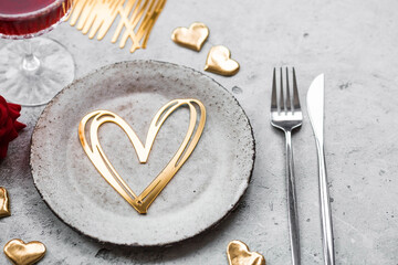 Obraz na płótnie Canvas The banner. Table setting. A stylish ceramic plate, a glass of red wine, a fork and gold, red hearts on a concrete background. The concept of celebrating Valentine's Day for cafes and restaurants.