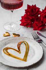 The banner. Table setting. Stylish ceramic plate, glass of red wine, red roses, fork and golden hearts on a concrete background. The concept of celebrating Valentine's Day for cafes and restaurants.