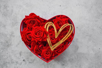 Valentine's day. Red roses and gold hearts in a heart-shaped box on a concrete background. A gift...