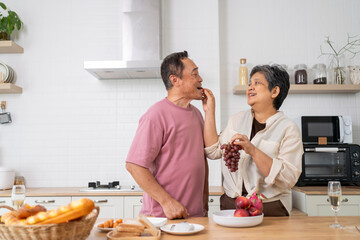 Mature asian Couples playfully tease each other with grapes in kitchen.