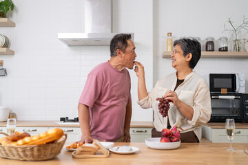 Mature asian Couples playfully tease each other with grapes in kitchen.