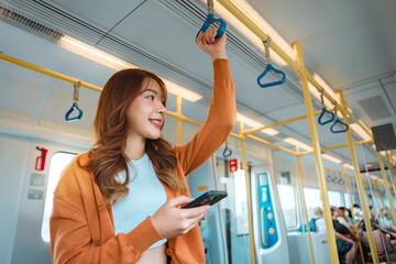 Happy young Asian woman passenger smile and using smart mobile phone in subway train station, lifestyle, transportation.