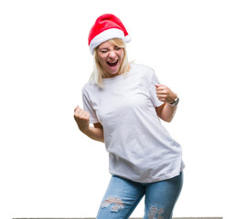 Young beautiful blonde woman wearing christmas hat over isolated background very happy and excited doing winner gesture with arms raised, smiling and screaming for success. Celebration concept.