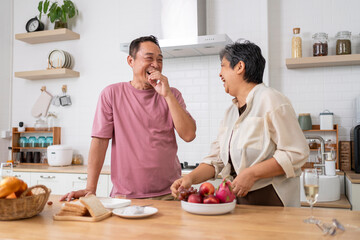 Mature asian Couples playfully tease each other with grapes in kitchen.