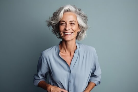 Portrait of a happy senior woman smiling while standing against grey background