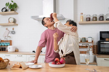 Mature asian Couples playfully tease each other with grapes in kitchen.