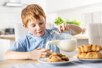 A little boy pours himself fresh milk during breakfast