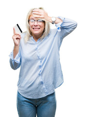Fototapeta premium Young beautiful blonde business woman holding credit card over isolated background stressed with hand on head, shocked with shame and surprise face, angry and frustrated. Fear and upset for mistake.