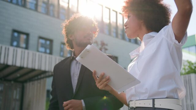 African American real estate manager realtor saleswoman businesswoman showing pointing at modern apartment office business city building skyscrapers talking to Indian man client dissatisfied reject