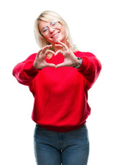 Young beautiful blonde woman wearing sweater and glasses over isolated background smiling in love showing heart symbol and shape with hands. Romantic concept.