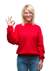 Young beautiful blonde woman wearing sweater and glasses over isolated background smiling positive doing ok sign with hand and fingers. Successful expression.