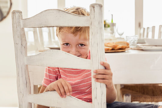 Young boy looking at the camera through his chair at the dinner table 