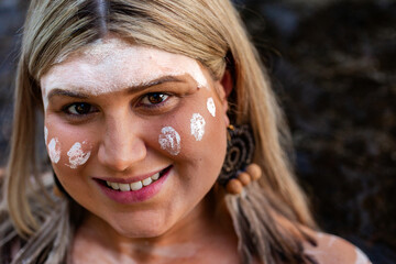 Close up portrait of aboriginal woman with woven earring and ochre paint on face