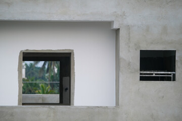 Window in the wall of a house under construction, concrete wall and window overlooking palm trees