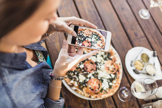 Beautiful happy woman taking a picture of her pizza at an outdoor restaurant.