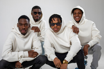 Group of African American guys in brown hoodies posing on a white background. Two in sunglasses.