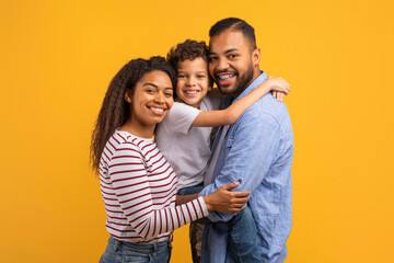 Portrait of cheerful black family with little son hugging and smiling