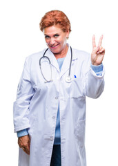 Senior caucasian doctor woman wearing medical uniform over isolated background smiling with happy face winking at the camera doing victory sign. Number two.