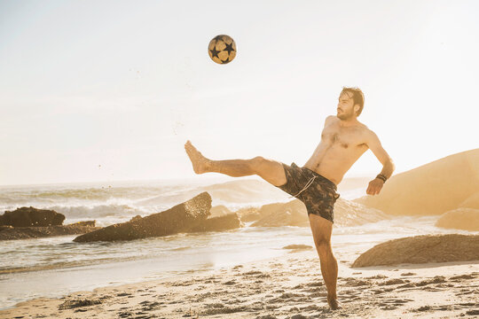 man playing with soccer ball on a beach at sunset