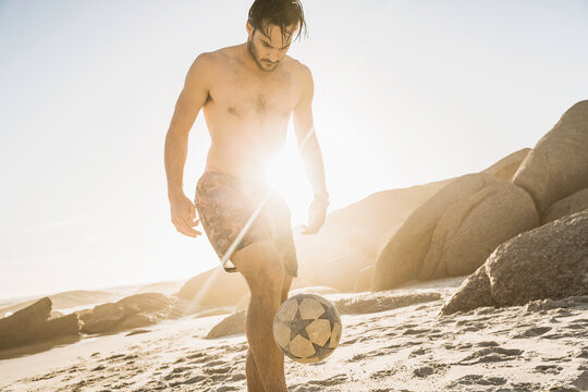 man playing with soccer ball on a beach at sunset