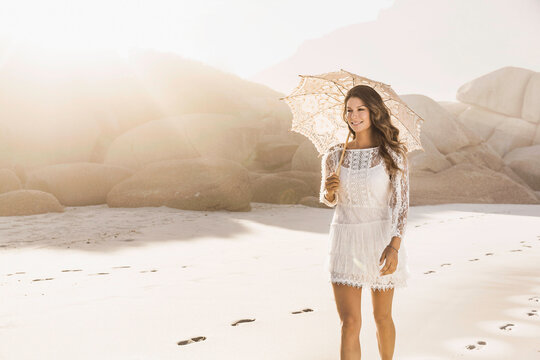 Beautiful girl in white summer dress dancing and playing on the beach