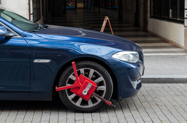 Red colored wheel clamp (wheel boot, parking boot) installed on a luxury car by police for law enforcement and parking violation in Czech Republic - obrazy, fototapety, plakaty