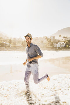 Man in pants and shirt walking and running along the beach