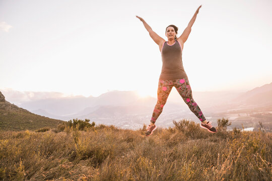 Beautiful overweight woman exercising on a mountain at sunset