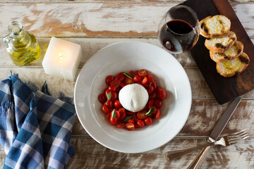 tomatoes with fresh cheese and olive oil, toasted bread on a board, glass of red wine, cutlery, for...