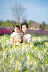 Fototapeta premium Mother and child in the flower field,Beautiful mother and daughter in spring poppy flower field. Mom holds her child daughter in the flowering meadow piggyback ride. Happy motherhood.