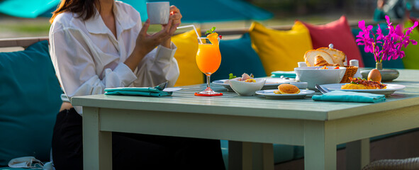 Woman drinking coffee and orange juice on the dining tableBuffet service. Tasty breakfast served on table. Travel woman in hat eating breakfast is served with eggs,