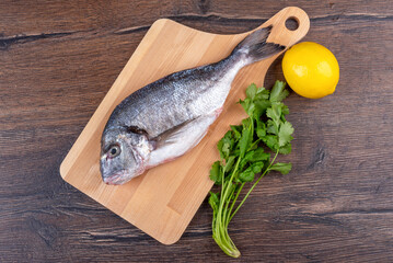 Top view of raw dorado fish on a cutting board, a bunch of cilantro and lemon.