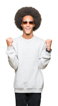 Young african american man with afro hair wearing sunglasses celebrating surprised and amazed for success with arms raised and open eyes. Winner concept.