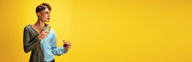 Banner. Soft and liquor drinks. Male model with make up man and woman holding glasses of champagne and whiskey against yellow background with copy space. Concept of self-expression, lifestyle. Ad