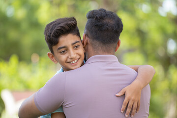 Cheerful indian son hugging or embracing to father at park - concept of relationship, fatherhood...