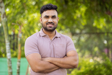 Happy smiling indian muscular man standing with crossed arms by looking at camera park - concept of Fitness Inspiration, Confident and Active Lifestyle