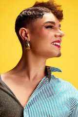 Profile portrait of model with female and male make up smiling turned head away against yellow...