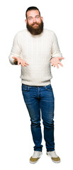 Young hipster man wearing winter sweater clueless and confused expression with arms and hands raised. Doubt concept.