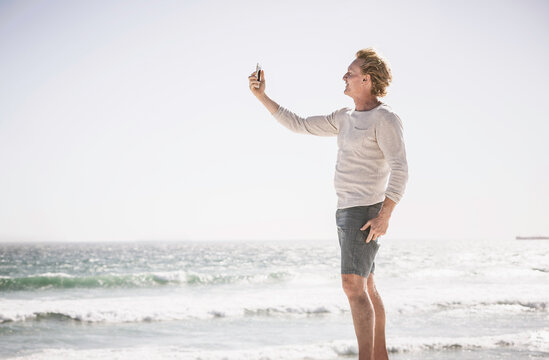 Man standing on the beach taking pictures with cell phone. Bloubergstrand, Capetown, South Africa