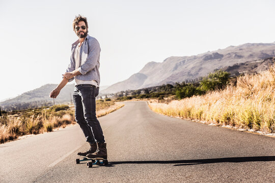 guy riding a skate board on the road in the countryside 