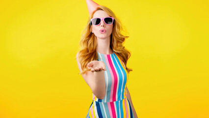 Wink, flirt and hipster woman sending air kiss and happy excited smiling. Fashionable lady blowing a kiss with confidence flirty emotion for cosmetics makeup, trendy outfit in studio yellow background - obrazy, fototapety, plakaty