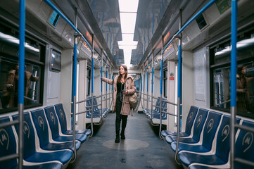 A young woman rides in a modern subway car with a phone in her hands. - obrazy, fototapety, plakaty
