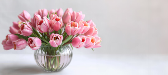Obraz na płótnie Canvas Delicate pink tulips in modern glass vase on light background 