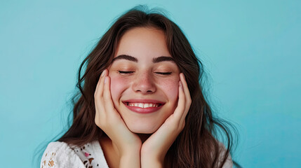 Naklejka premium Cheerful female smiling for camera and clasping hands under cheek while pretending to sleep against blue background